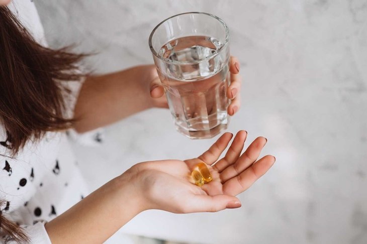 Diet. Nutrition. Girl's hands with pills with cod liver omega-3 oil and a glass of fresh water. The concept of a healthy diet and lifestyle. Vitamin D, E, fish oil capsules.
